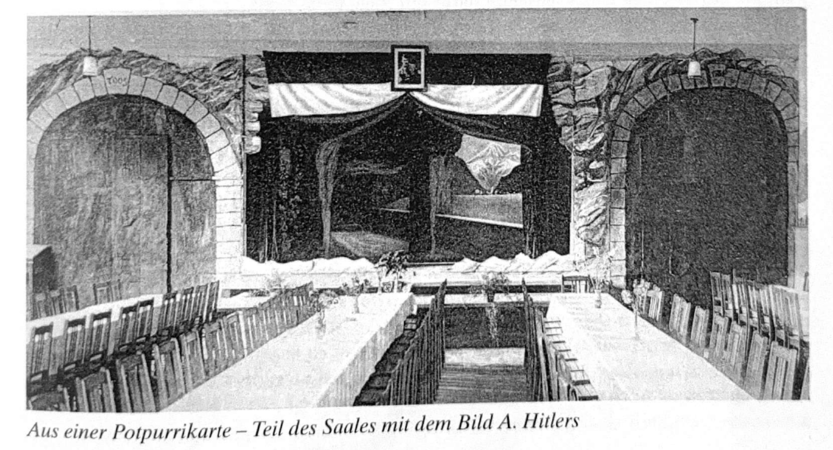 Der Raum zeigt eine lange Festtafel mit Stühlen unter einem gemalten Felsbogen und einem zentralen Wandbild, das von Vorhängen umrahmt ist.