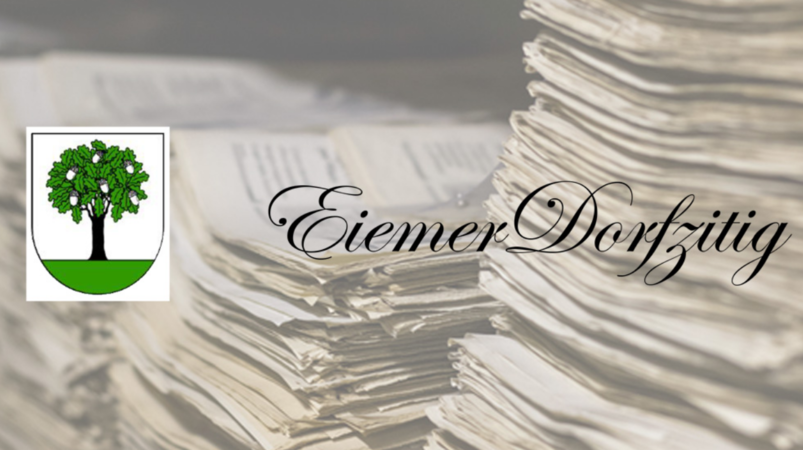 Die Eiemer Dorfzitig: Ein Stapel alter Zeitungen liegt auf einem Tisch, daneben befindet sich ein Wappen mit einem Baum und der Schriftzug "Eiemer Dorfzitig".