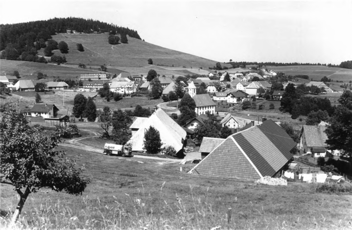 Foto von Ingrid Schubert: Gersbach 1983. Eine Landschaftsansicht zeigt ein Dorf mit mehreren Häusern und einem Hügel im Hintergrund in einer ländlichen Umgebung.