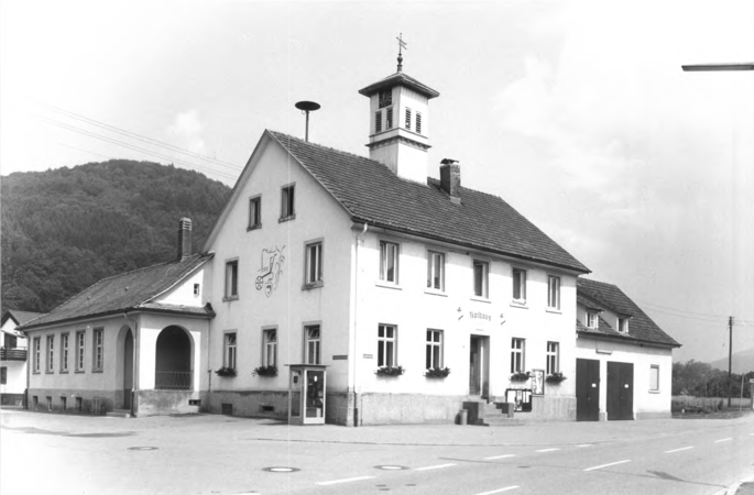 Foto von Ingrid Schubert: Langenau 1983. Das Bild zeigt ein historisches, zweistöckiges Gebäude mit der Aufschrift "Rathaus", einem Glockenturm und Dekorationen an der Fassade.
